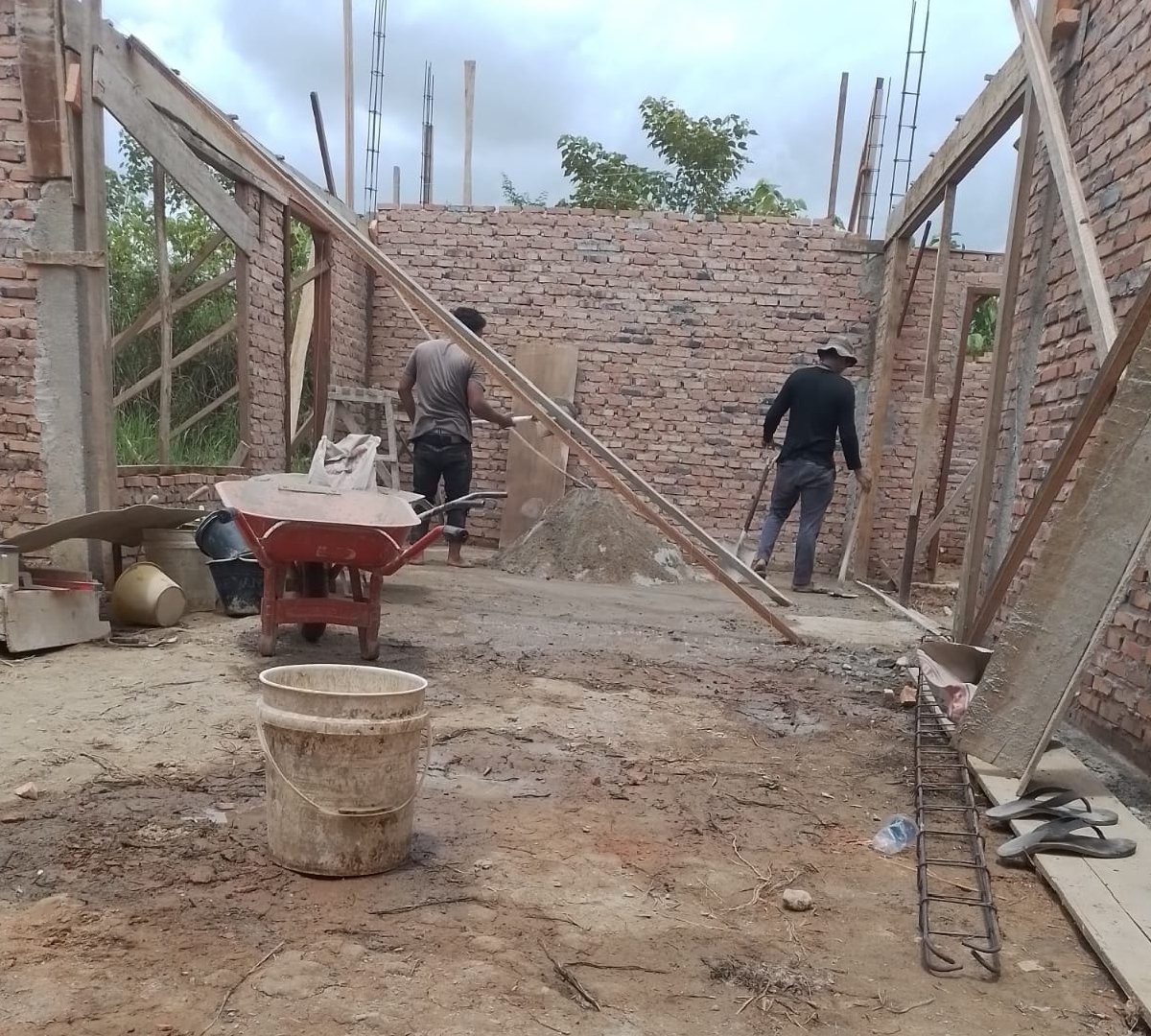 Pekerja bangunan sedang mengerjakan plester aci pada dinding dengan teknik rapi dan halus.